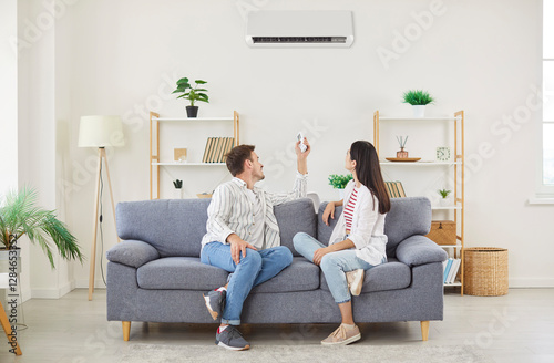 Climate control, couple air conditioner fixing sitting relaxing on sofa holding controller, regulate climate at home using modern ac device, home ventilation to cool or warm new living room flat  photo