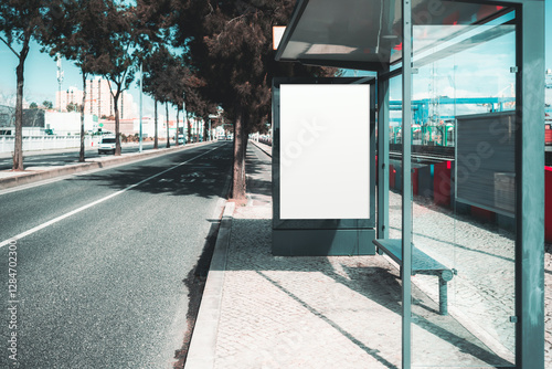 Blank advertising billboard mockup at a modern bus stop with glass walls. Urban street with bicycle lane, trees, and buildings in the background. Ideal for ad design. An outdoor ad banner template