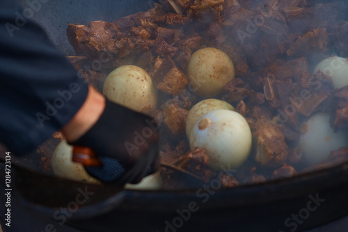 Beef meat is fried with onions in a large cauldron. Cooking national Asian meat soup with vegetables. Thick steam. Selective focus.