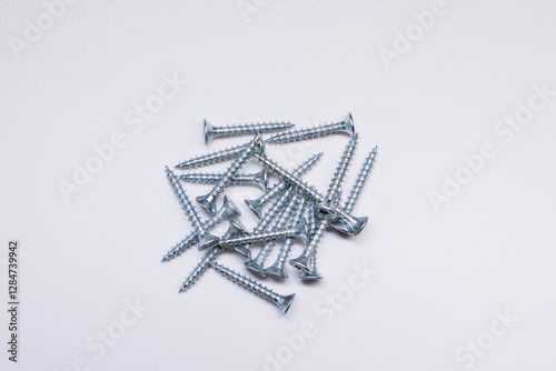 A collection of uniformly sized silver screws with sharp threads and flat countersunk heads arranged on a clean white background.