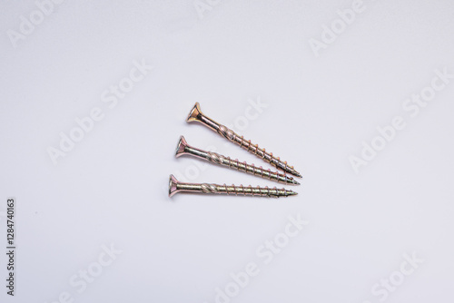 Three golden screws with spiral threads and flat countersunk heads are arranged diagonally on a white background, emphasizing their reflective surface.