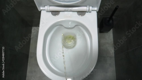 Bright yellow stream of urine pours into pristine white ceramic toilet, set in elegant modern bathroom with dark grey tiled walls and pristine interior design. First-person view.