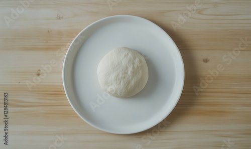 Minimalist white plate with freshly made dough placed on a light wooden table, natural light creating a clean and inviting baking scene