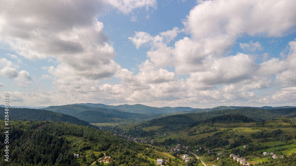 Obraz premium Majestic Mountains, Lush Green Forests, And Soft White Clouds On A Sunny Day. Aerial View Showcasing The Stunning Beauty Of Nature From A High Perspective.