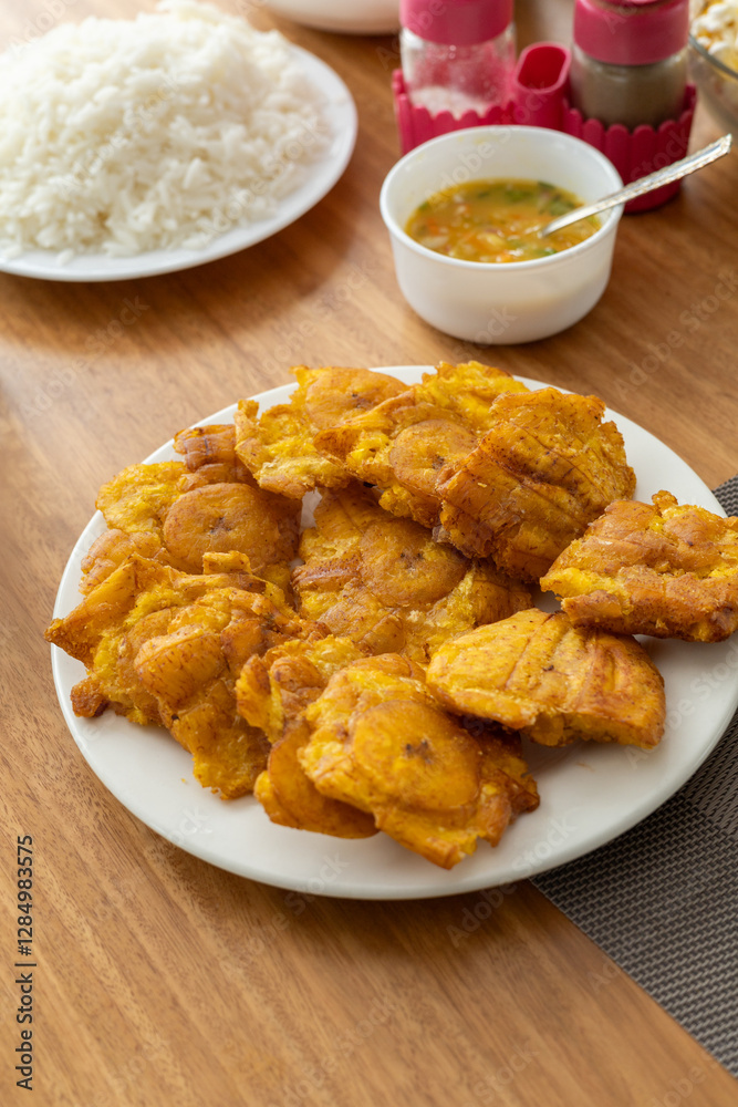 Crispy fried patacones served on a table with a portion of rice and spicy hot sauce, perfect for food, cuisine, and traditional dish-themed content. Crispy fried patacones served on a table with a portion of rice and spicy hot sauce, perfect for food, cuisine, and traditional dish-themed content.