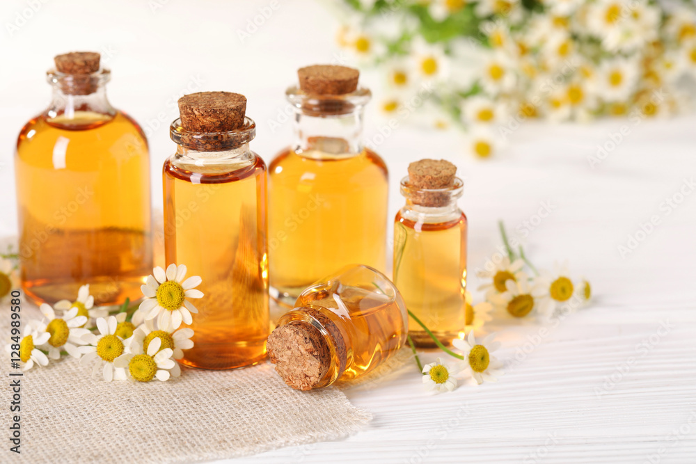 Bottles of essential oil and chamomile flowers on white wooden table, closeup Bottles of essential oil and chamomile flowers on white wooden table, closeup