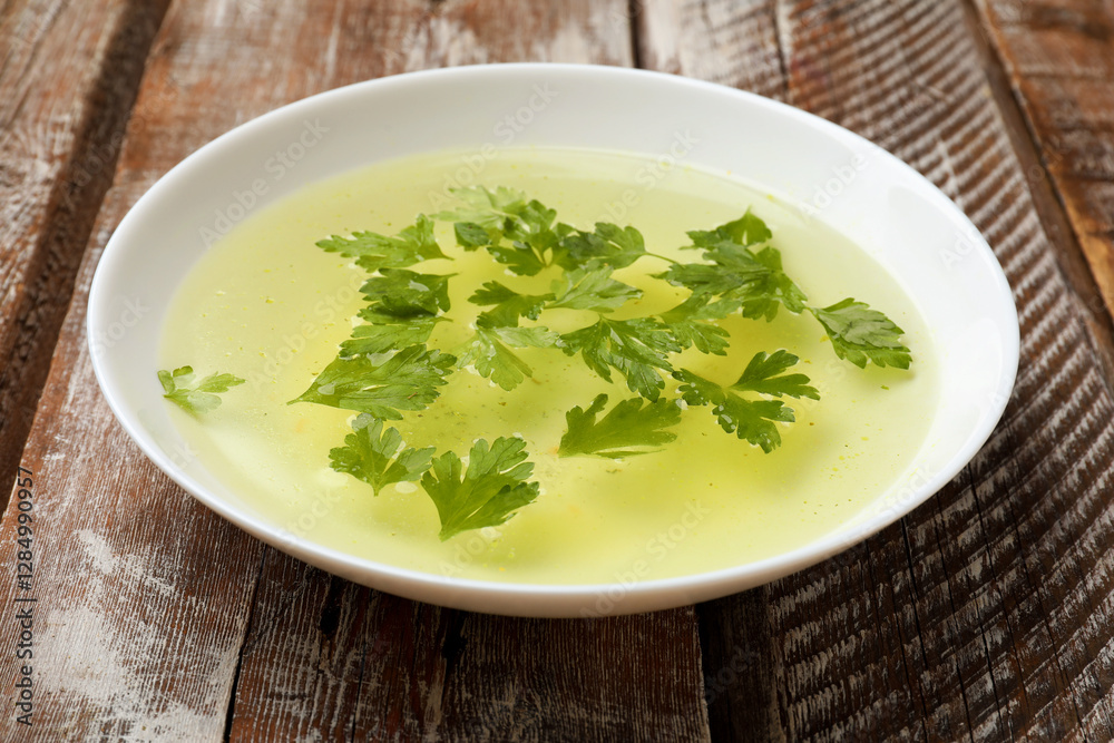 Tasty chicken bouillon with parsley in bowl on wooden table, closeup Tasty chicken bouillon with parsley in bowl on wooden table, closeup