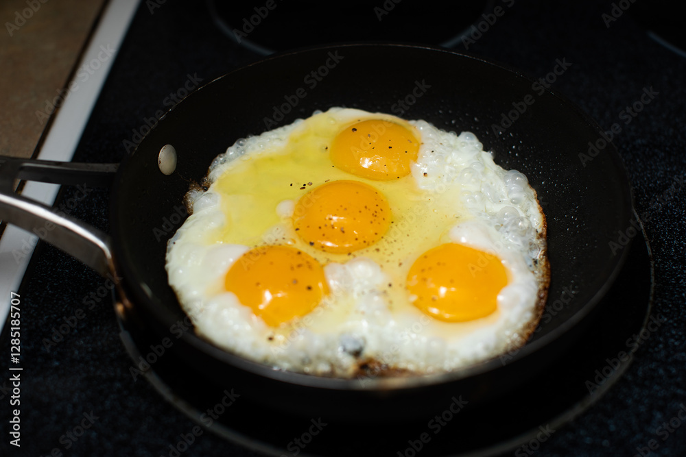 four almost fried eggs in cooking in a black pan on the stove four almost fried eggs in cooking in a black pan on the stove