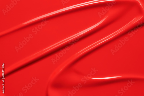 Red lipstick texture background. Creamy makeup product or paint swatch. Bright color liquid lipstick or lip gloss smeared