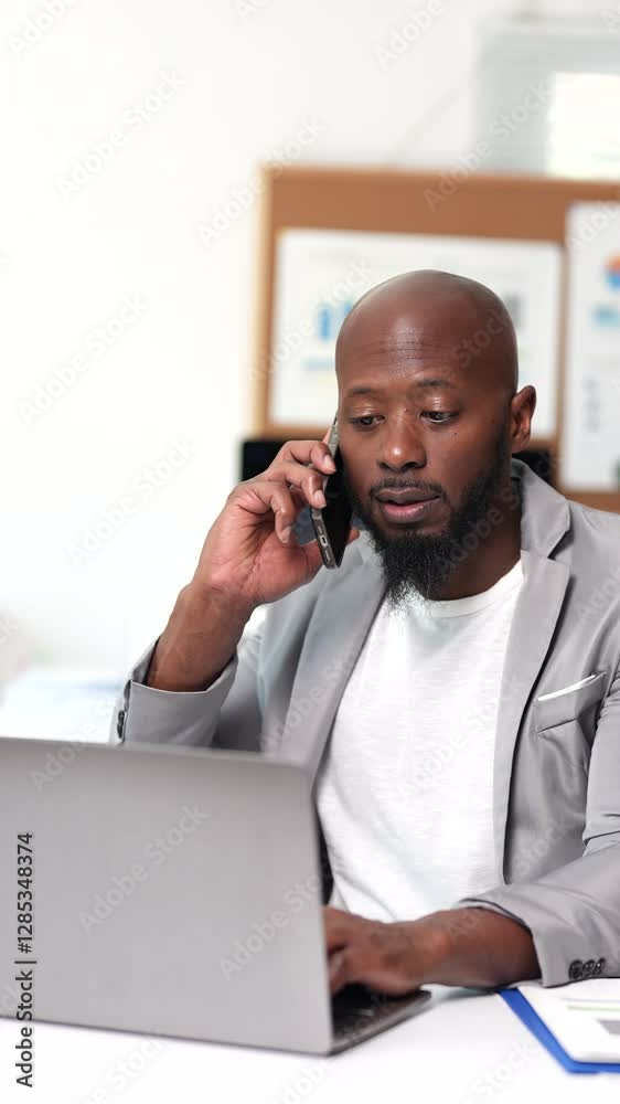 Professional businessman managing multiple business tasks, working on laptop while handling phone conversation in modern, well-organized office environment with focused, confident demeanor Professional businessman managing multiple business tasks, working on laptop while handling phone conversation in modern, well-organized office environment with focused, confident demeanor
