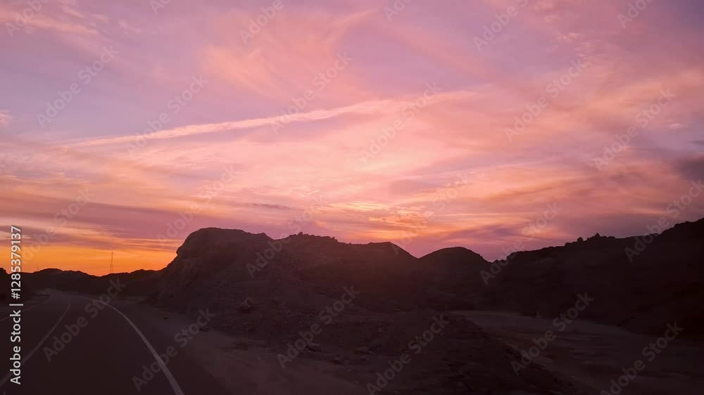 A vibrant orange sky at dusk with dark mountain silhouettes, along a road from Luxor to Hurghada, Egypt. The serene desert landscape is captured from a bus journey. A vibrant orange sky at dusk with dark mountain silhouettes, along a road from Luxor to Hurghada, Egypt. The serene desert landscape is captured from a bus journey.
