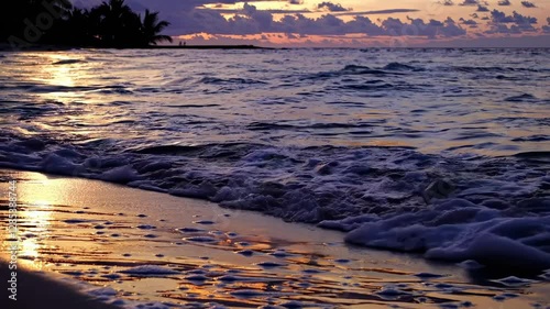 A serene beach sunset video with gentle waves lapping the shore. Captured from a low angle, highlighting the vibrant sky and reflective water.