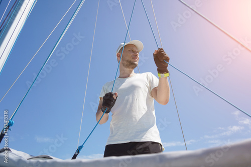 Foto Male captain on deck of sailboat opening sails pulling the rope