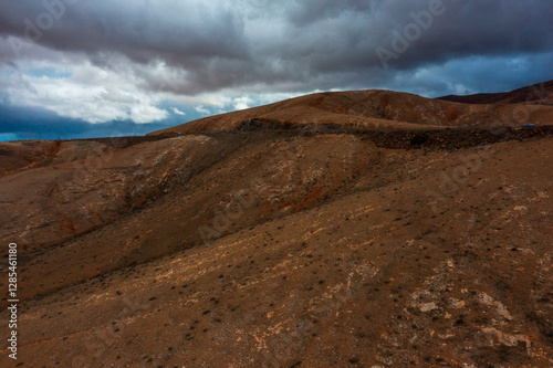 Dramatic storm clouds over Fuerteventura's rust-coloured volcanic landscape. Dark sky contrasts with barren mountains showing the raw geological beauty of this Canary Island