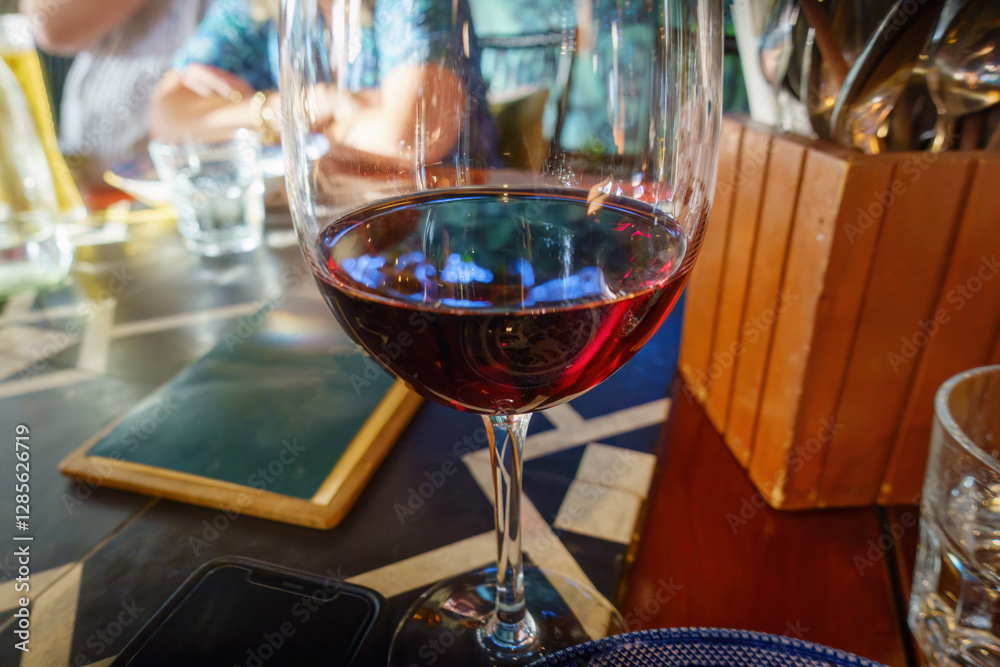 Red wine glass in a restaurant. Unrecognizable people in the background. Auckland.