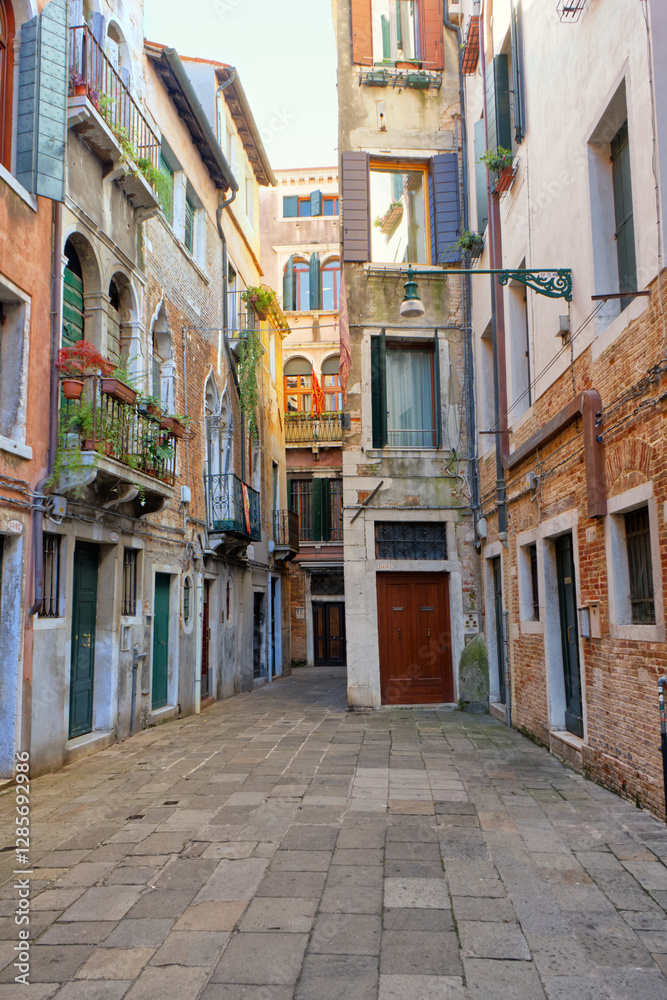 Fototapeta premium A quiet Venetian alleyway, paved with stone, winds between aged buildings, revealing the city's charming, intimate architecture and hidden corners.