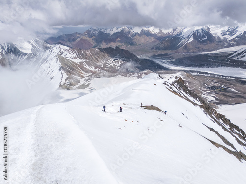 Mountaineers descending from summit amongst snow and alpine landscape, Pamir Mountains, Kyrgyzstan