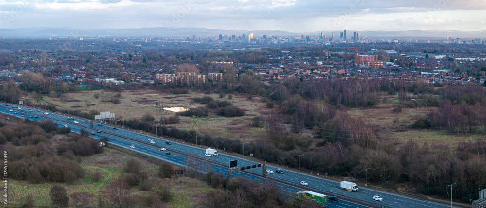 Fototapeta premium Panoramic aerial image of M60 Manchester outer ring road near Swinton with Manchester skyline on the horizon. 