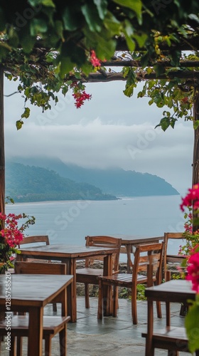 Scenic coastal view with wooden seating and floral canopy on a misty day