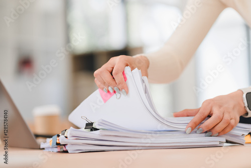 Person organizing stack of documents on desk, with laptop and coffee cup in background.