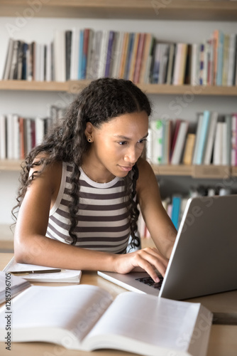 Focused African student girl studying online using laptop, review new task, learns through educational platform, reading topics, busy in reference material gathering for diploma use internet resources
