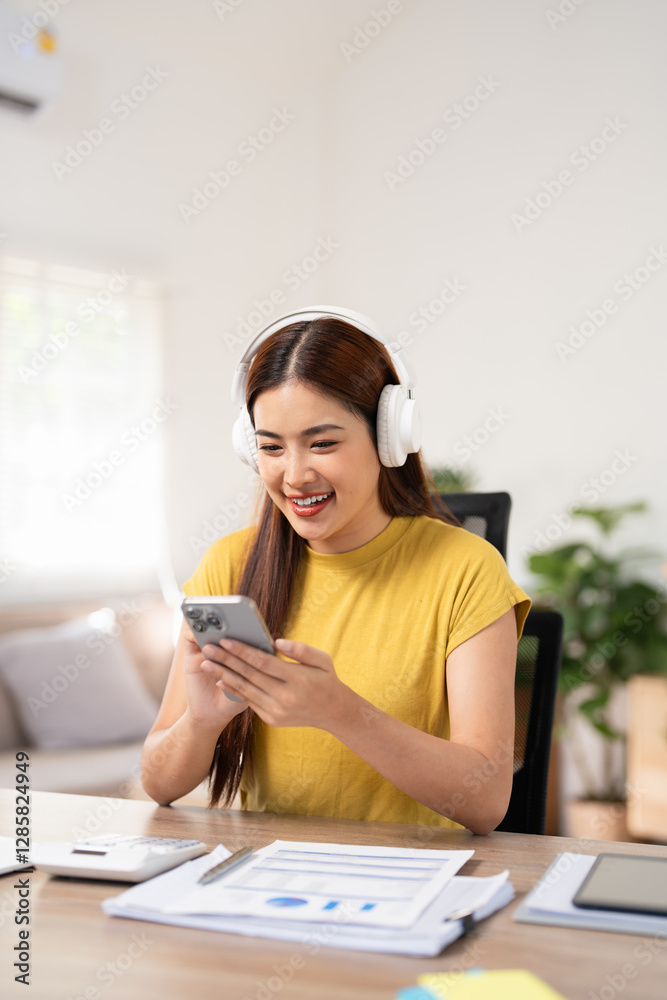 Smiling woman working at cozy home office, wearing headphones listening music at home using mobile phone remote work. Remote work concept. Smiling woman working at cozy home office, wearing headphones listening music at home using mobile phone remote work. Remote work concept.