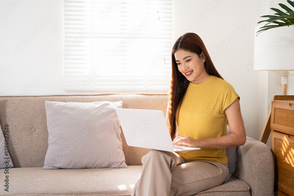 Smiling asian woman using laptop while sitting on couch at home. Happy female shopping or chatting online in social network, typing blog, freelancer working on a project. Smiling asian woman using laptop while sitting on couch at home. Happy female shopping or chatting online in social network, typing blog, freelancer working on a project.