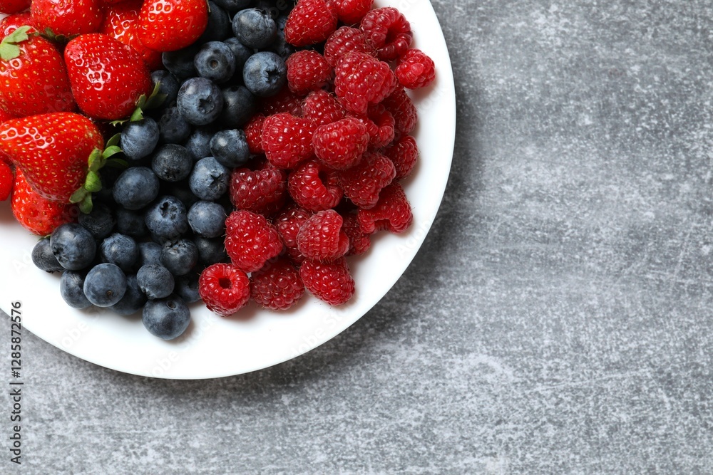 Different fresh ripe berries in bowl on gray table, top view Different fresh ripe berries in bowl on gray table, top view