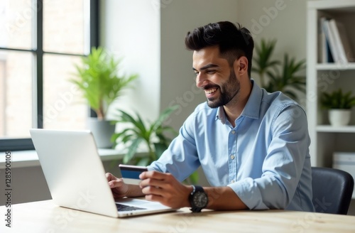 An Indian man is sitting at a table in front of a computer with a bank card in his hands, paying for an online purchase. A bargain, a sale