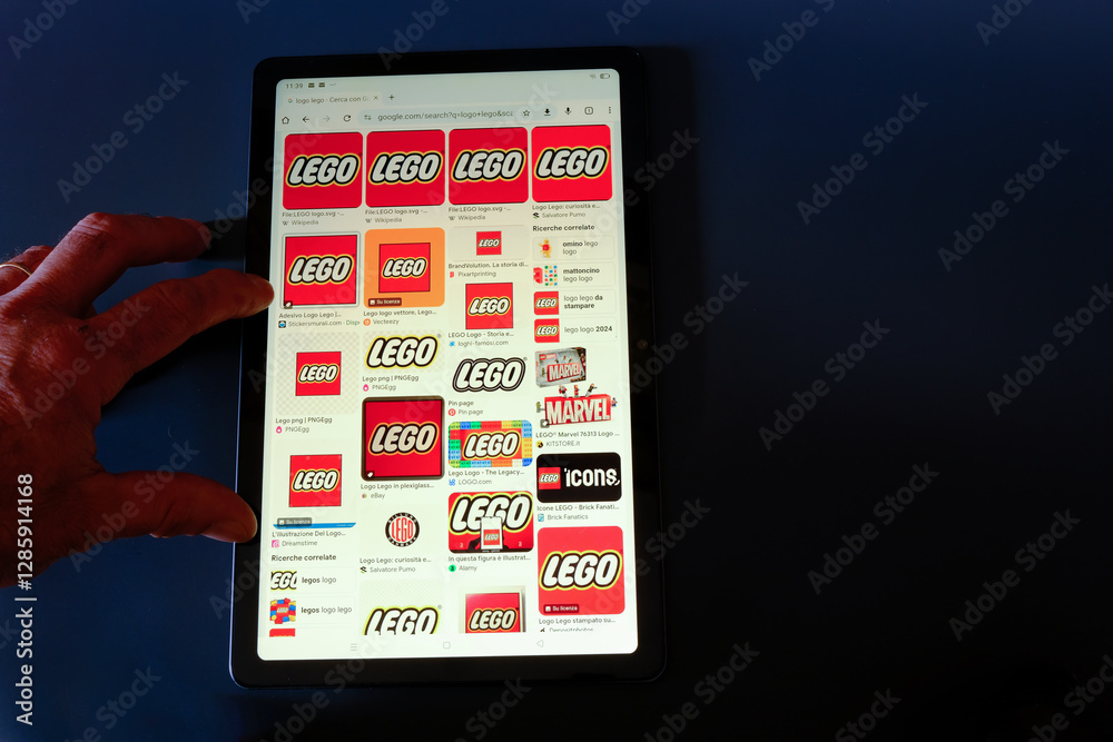 Naklejka premium Hand holding tablet, on LEGO icon on black background, February 21, 2025