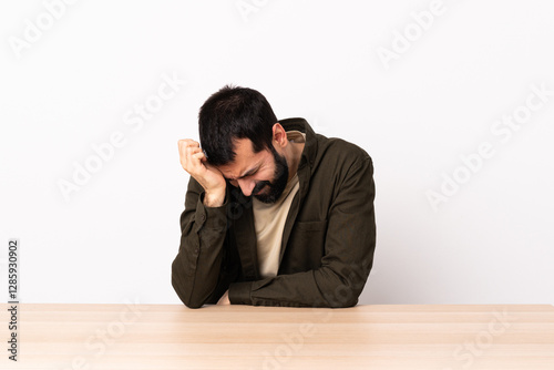 Caucasian man with beard in a table with headache.