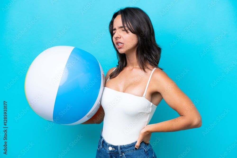 Young hispanic woman holding beach ball isolated on blue background suffering from backache for having made an effort Young hispanic woman holding beach ball isolated on blue background suffering from backache for having made an effort