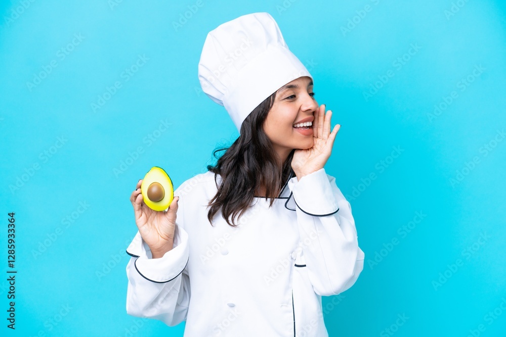 Young hispanic chef woman holding avocado isolated on blue background shouting with mouth wide open to the side Young hispanic chef woman holding avocado isolated on blue background shouting with mouth wide open to the side