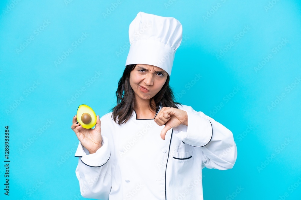 Young hispanic chef woman holding avocado isolated on blue background showing thumb down with negative expression Young hispanic chef woman holding avocado isolated on blue background showing thumb down with negative expression