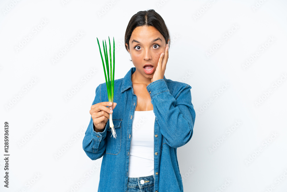 Young hispanic woman holding chive isolated on white background with surprise and shocked facial expression Young hispanic woman holding chive isolated on white background with surprise and shocked facial expression