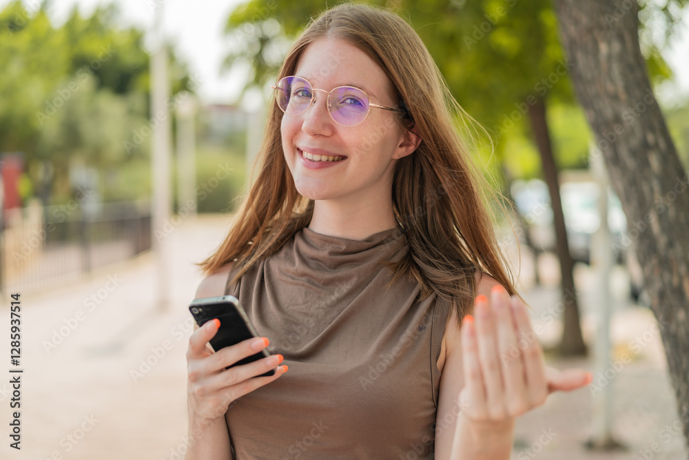French girl with glasses using mobile phone at outdoors inviting to come with hand. Happy that you came French girl with glasses using mobile phone at outdoors inviting to come with hand. Happy that you came