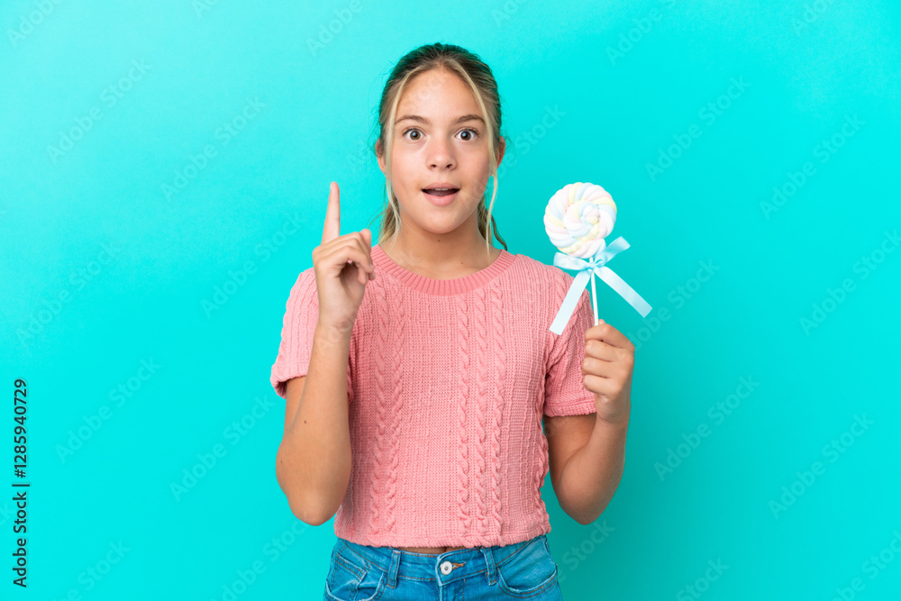 Little Caucasian girl holding a lollipop isolated on blue background thinking an idea pointing the finger up Little Caucasian girl holding a lollipop isolated on blue background thinking an idea pointing the finger up