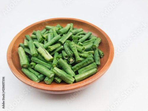 Long beans (Vigna Unguiculata ssp. Sesquipedalis) that have been cut into pieces in a wooden bowl on a white background.