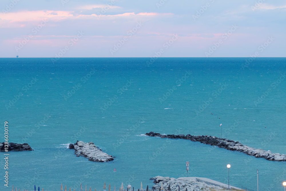 Fototapeta premium blue sea and pink sky during a storm, stormy sea, blue sea, purple sky, azure blue, empty sandy beach during a storm, breakwater and high waves, splashing waves