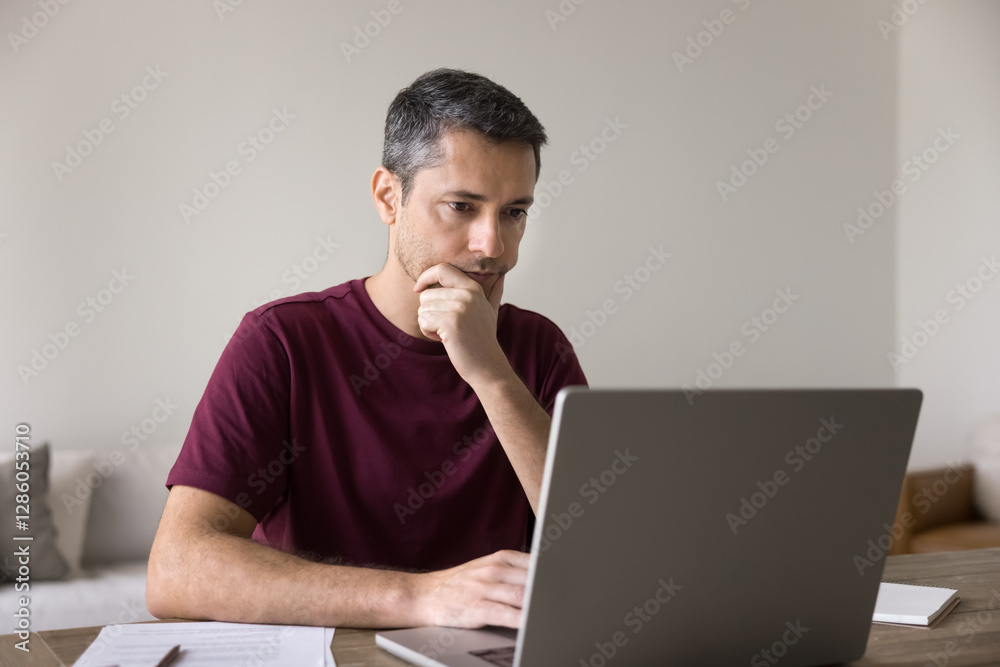 Middle-aged man sits at desk, thoughtfully examining received e-mail or message working on laptop with contemplative expression, learn new platform, in deep concentration, solve problem, analyze data Middle-aged man sits at desk, thoughtfully examining received e-mail or message working on laptop with contemplative expression, learn new platform, in deep concentration, solve problem, analyze data