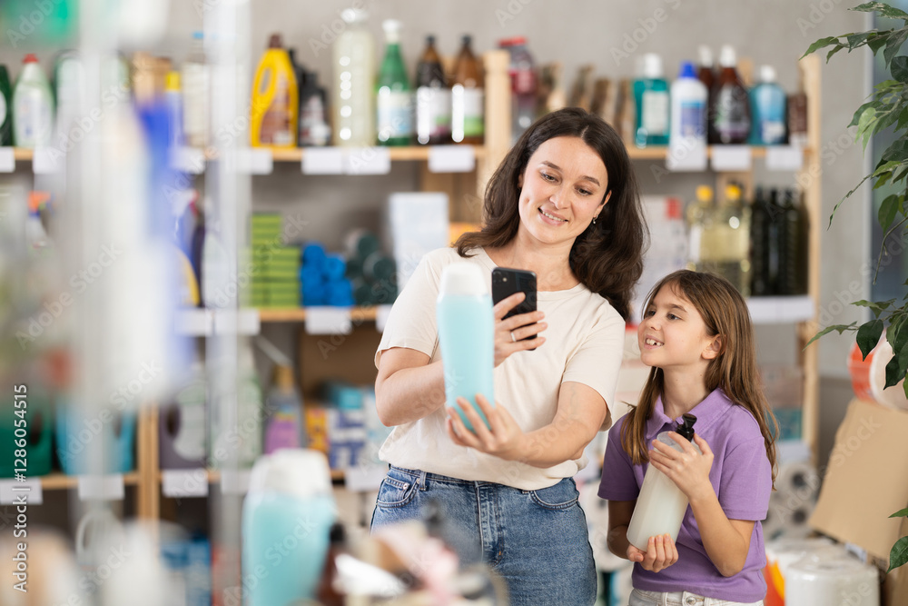 Mother and daughter checking expiration date of shampoo or shower gel using her smartphone in household supermarket Mother and daughter checking expiration date of shampoo or shower gel using her smartphone in household supermarket
