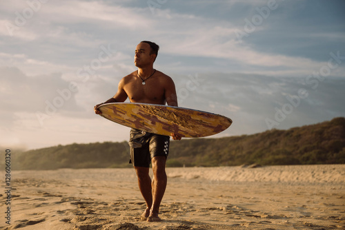 Surfer waiting for the perfect waves on the beach at sunset holding skimboard photo