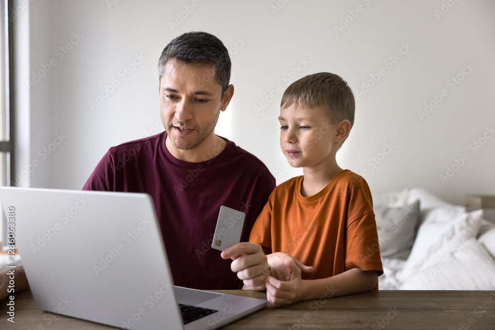 Young father and little son buying goods, e-services at home using card and laptop, do e-shopping, purchasing products from ecommerce platforms, pay for online game, streaming subscriptions services Young father and little son buying goods, e-services at home using card and laptop, do e-shopping, purchasing products from ecommerce platforms, pay for online game, streaming subscriptions services
