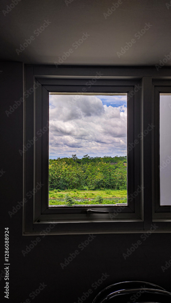 Fototapeta premium A beautifully framed view of lush greenery and a cloudy blue sky seen through a modern window. 