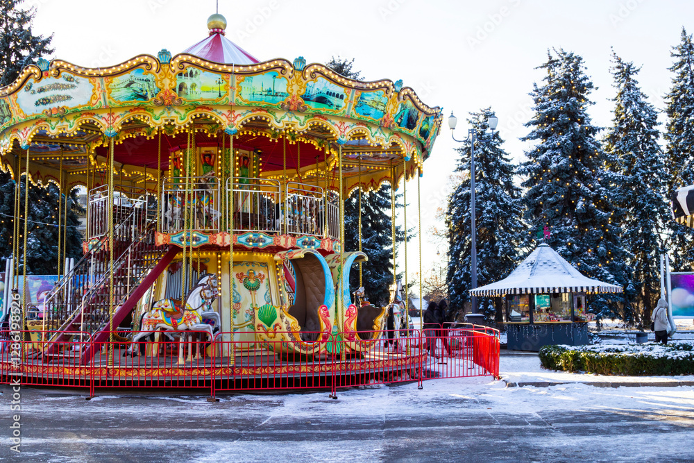 Children's carousel in the city park. Lighting garlands on the trees. Snow on the ground