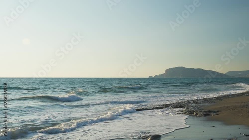 A breathtaking slow motion still shot capturing a tranquil beach during sunset, with the sun casting warm golden light from the side. Gentle waves roll onto the shore