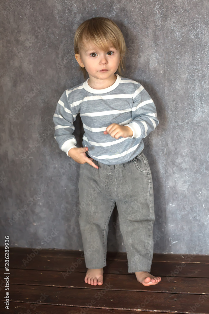 a handsome blond boy with big brown eyes in a gray sweatshirt and jeans on a gray background a handsome blond boy with big brown eyes in a gray sweatshirt and jeans on a gray background
