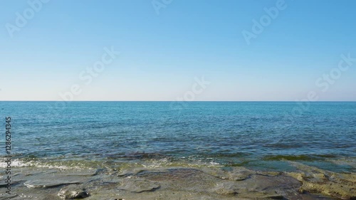 A captivating slow motion still shot of ocean waves crashing against the coastal rocks and beach during the daytime