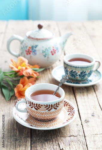 A beautiful ceramic cups and saucers with tea on a old wooden table with tea pot. Selective focus.