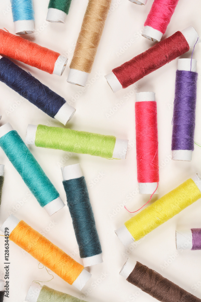 Fototapeta premium A top-down, flat lay shot of numerous spools of colorful thread scattered randomly on a light background, showcasing a variety of hues and textures